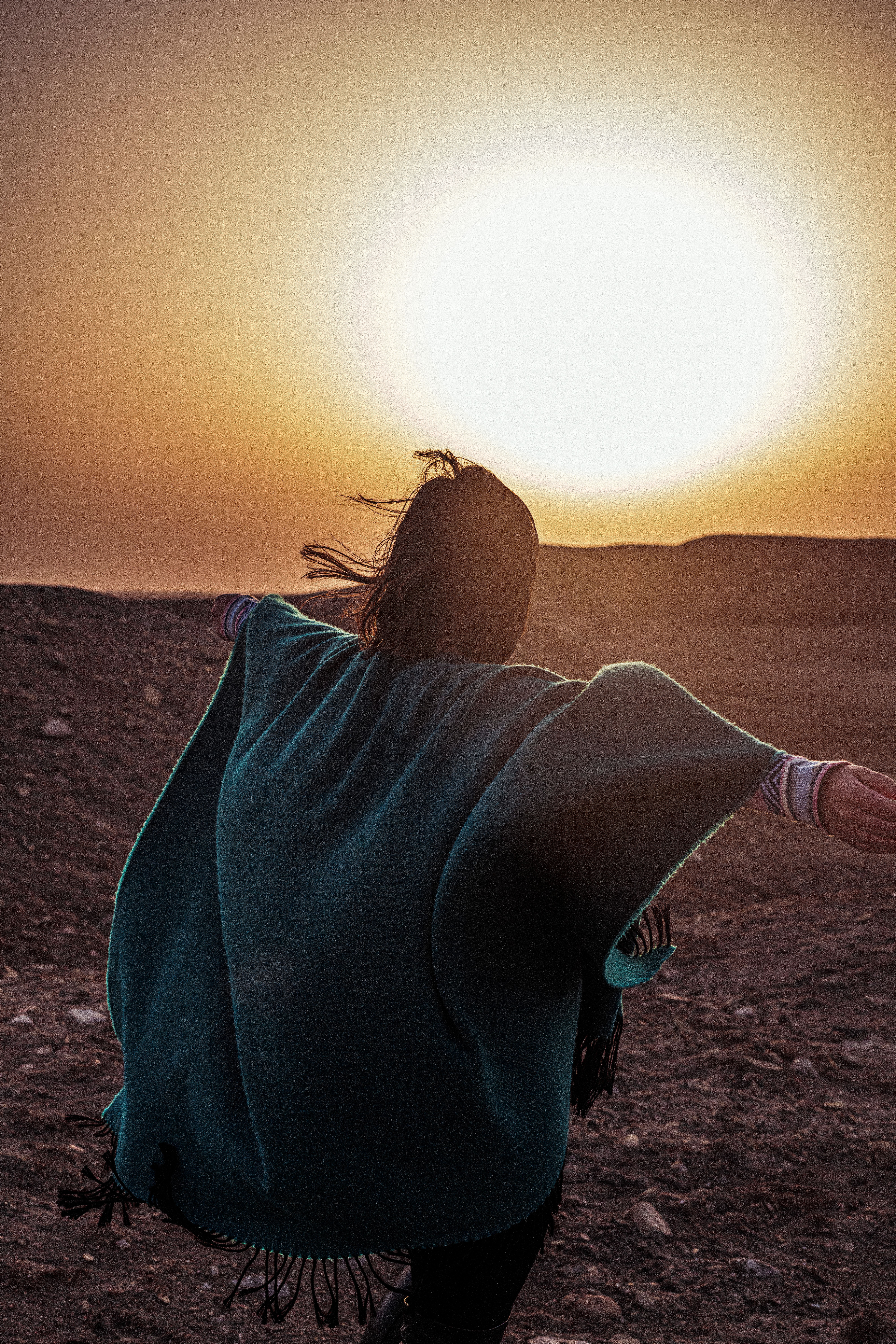 A woman in a poncho embraces the desert at sunset in Amarah, Iraq, arms outstretched.