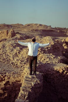 A man with outstretched arms stands in a historic desert landscape near Baghdad, Iraq.