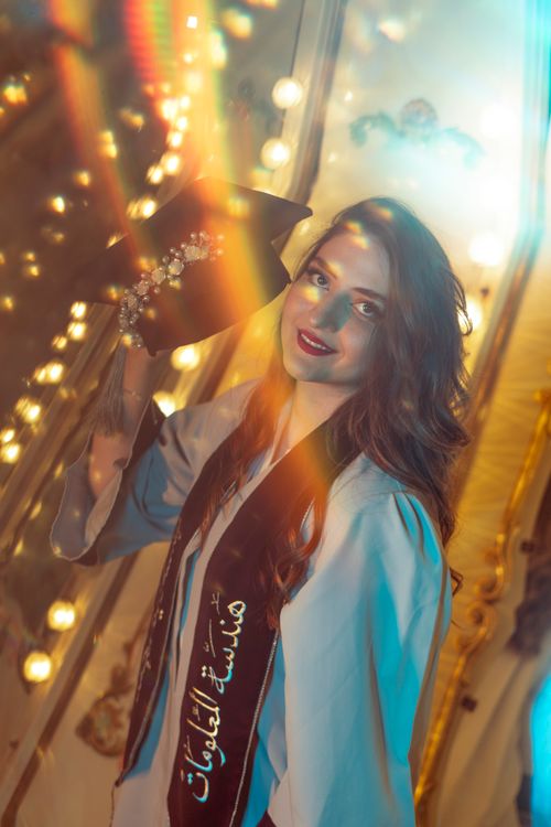 Free Young woman celebrating graduation with cap and gown in a vibrant, whimsical setting. Stock Photo