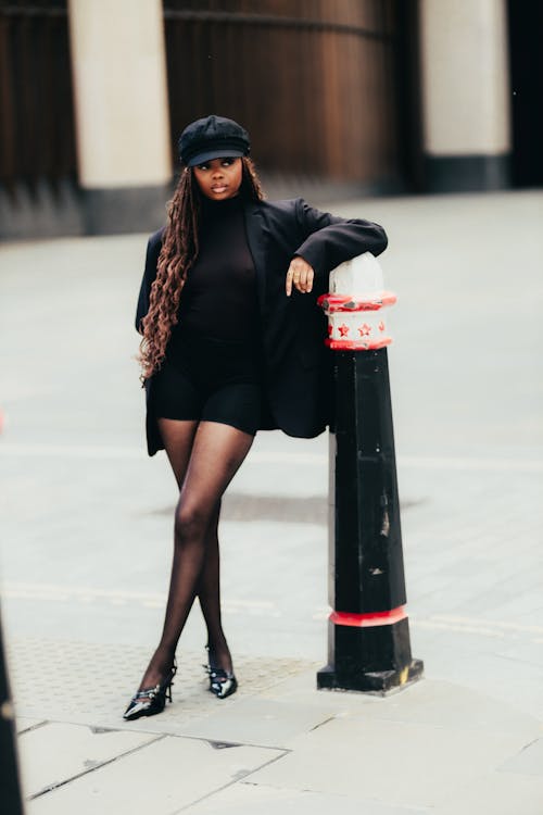 A woman in black stockings and a hat leaning against a pole