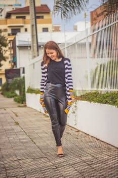 一位穿着时尚休闲服的年轻女子在阳光明媚的城市人行道上散步微笑