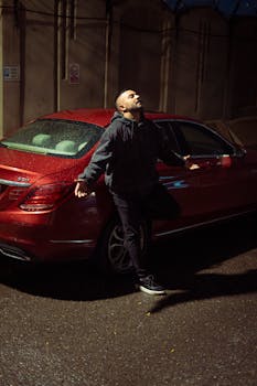 A man stands by a red car in the rain at night in Tokyo. Urban ambiance captured beautifully.