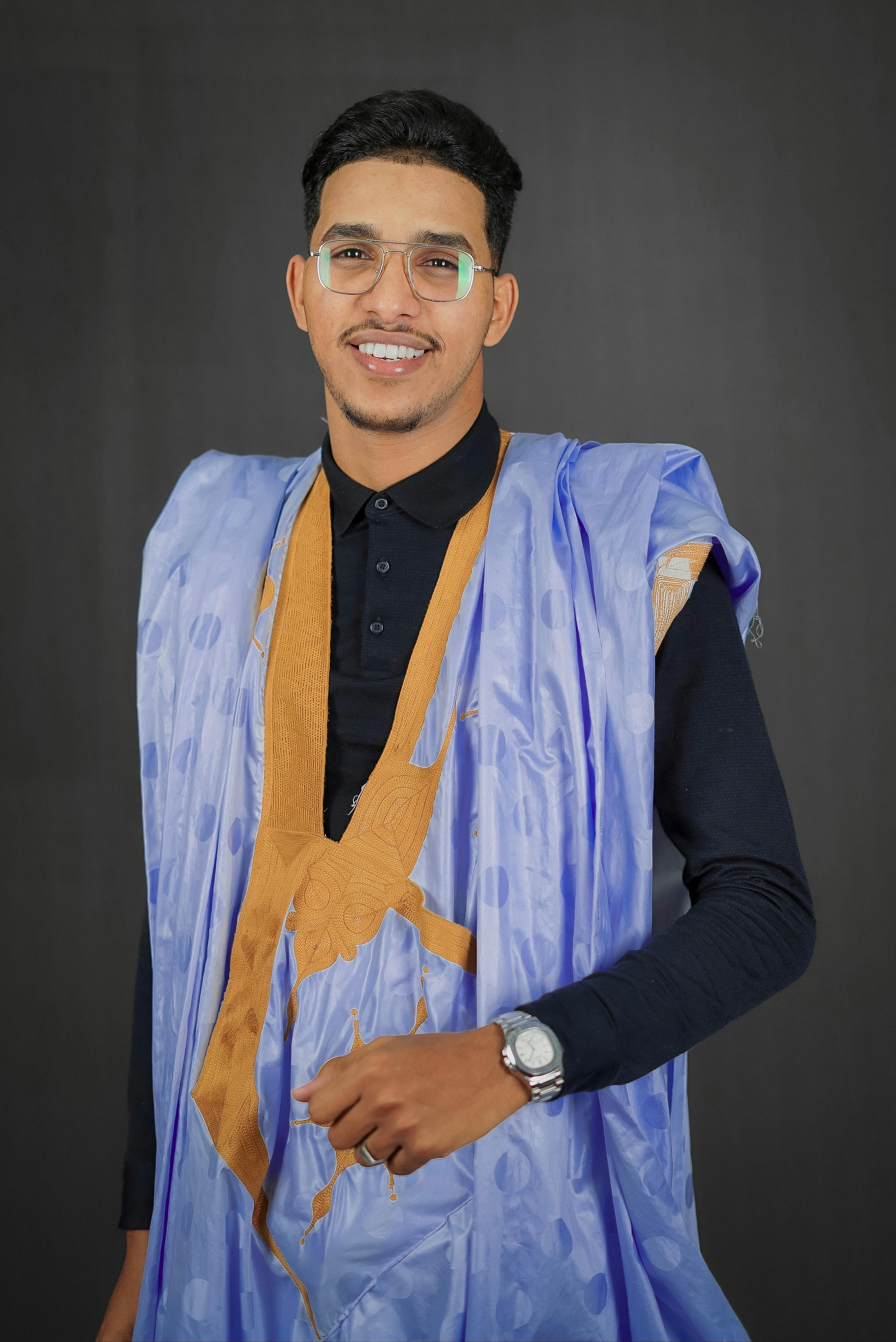 Portrait of a smiling man wearing traditional blue and orange attire, posing confidently in a studio.