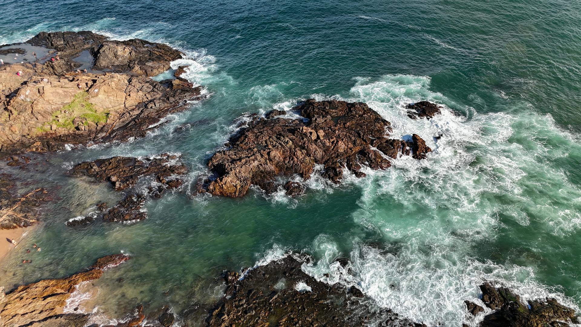 Aerial shot of the rocky coastline in Salvador, Brazil, with waves crashing against the rocks.