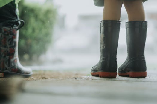 Two children standing in the rain wearing boots, emphasizing rainy weather and playful mood.
