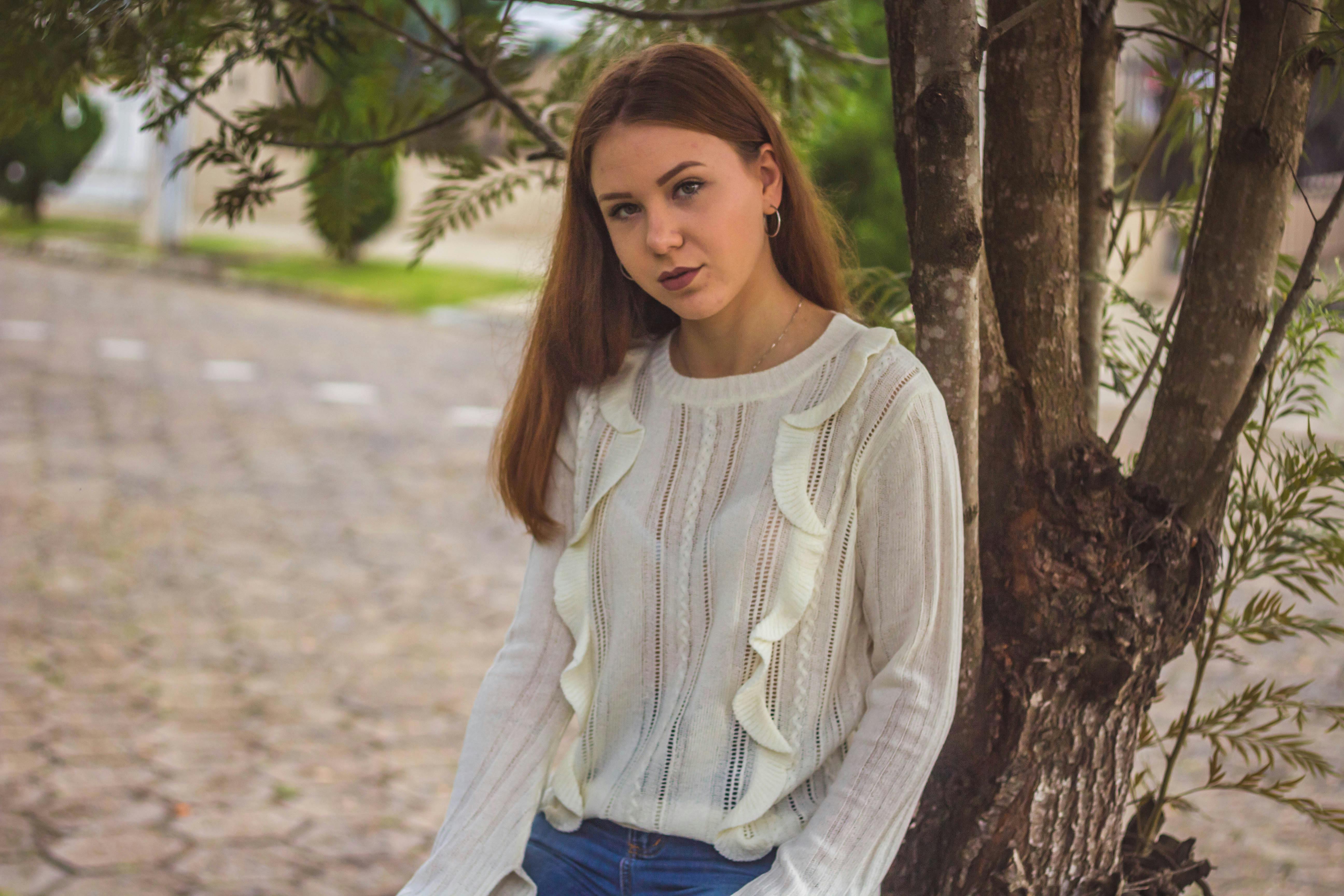 一位穿着白色毛衣的女人坐在树旁的户外肖像