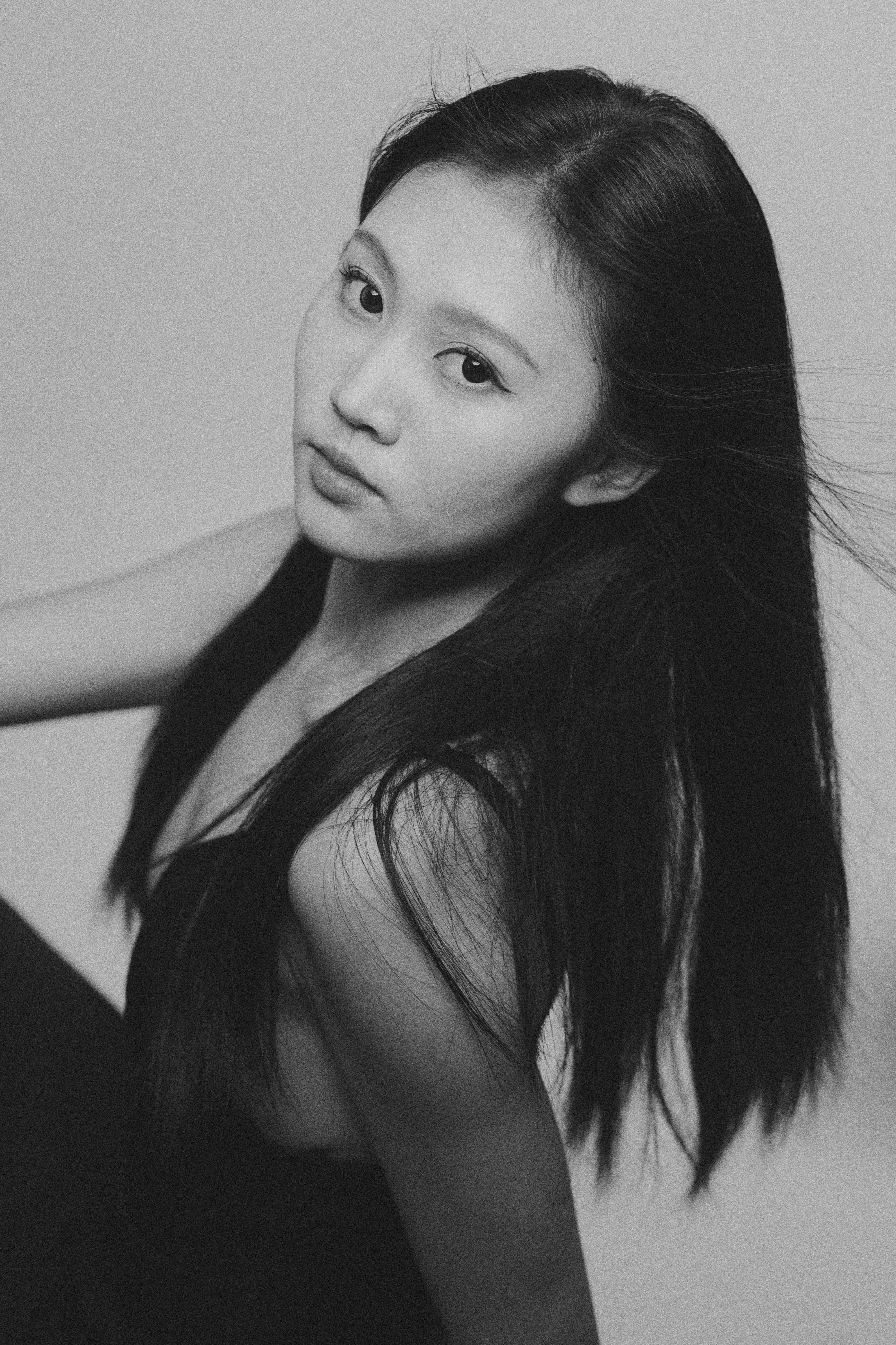 Artistic black and white portrait of an Asian woman with long hair in a studio setting.