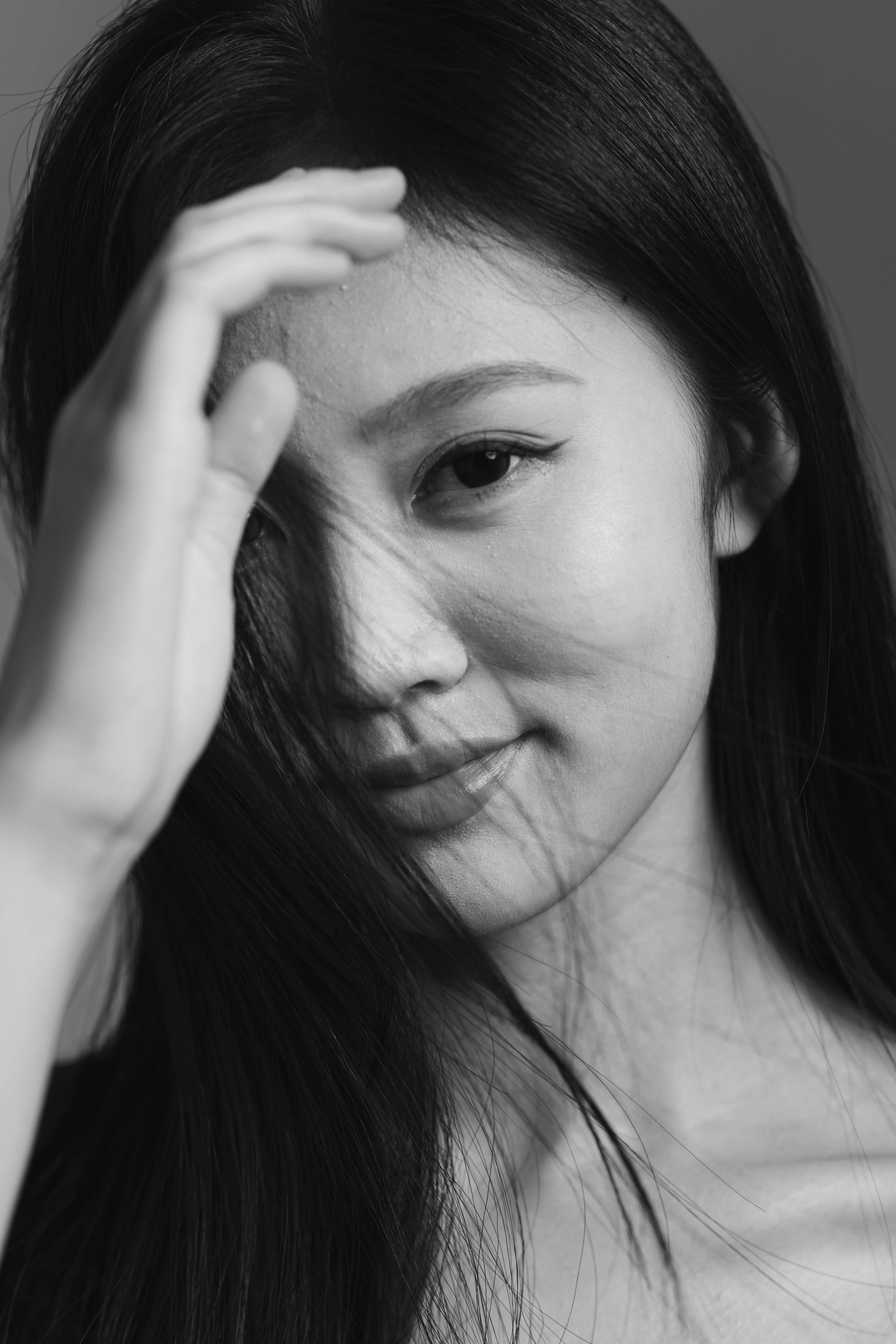A captivating black and white portrait of an Asian woman with a serene expression, touching her hair.