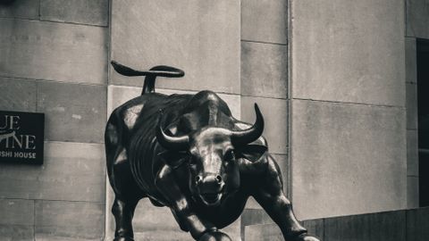 Black and white image of the Charging Bull statue in a cityscape, symbolizing strength and finance.