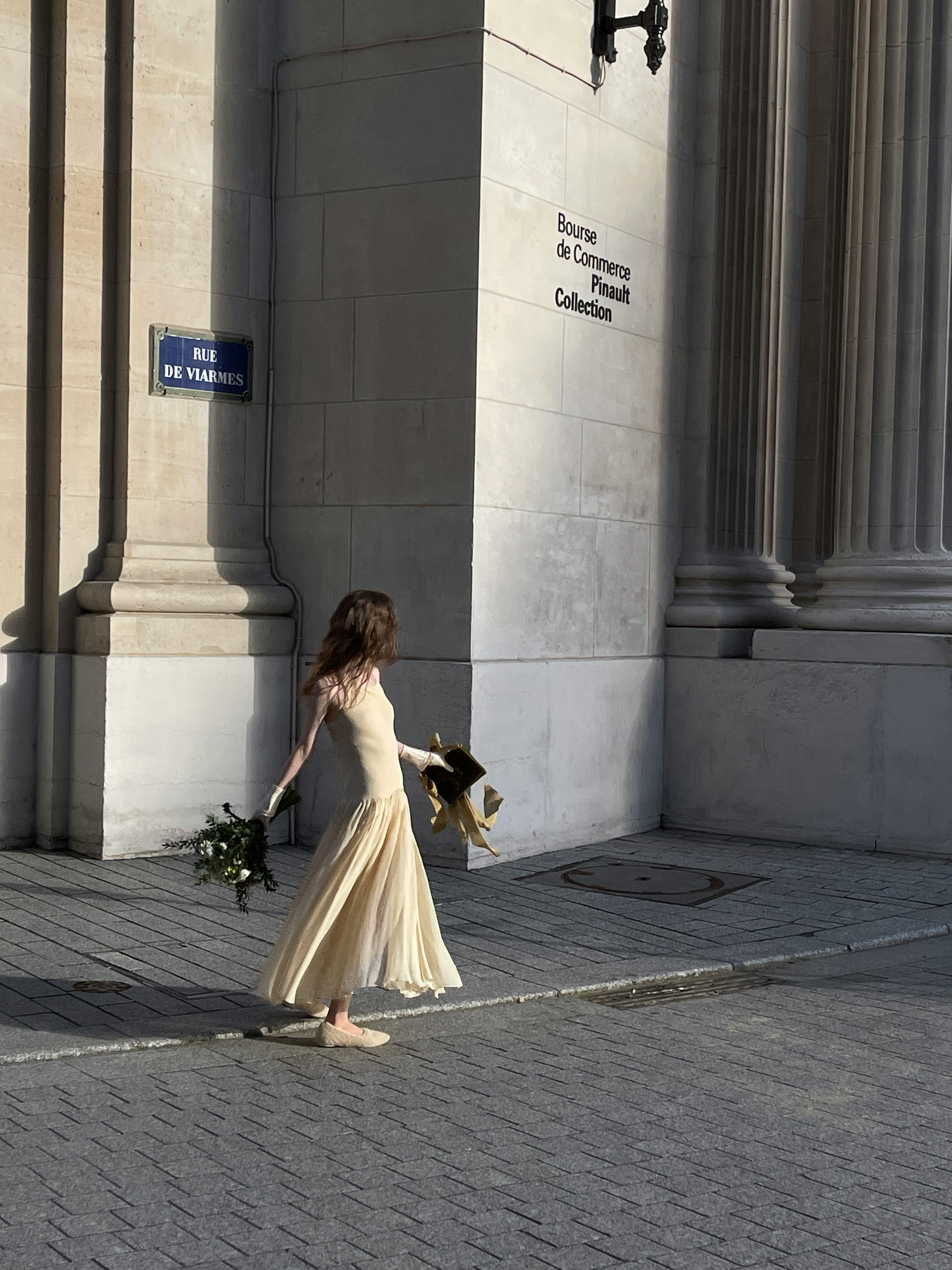 A woman in a yellow dress holding flowers in front of the Bourse de Commerce, Paris.