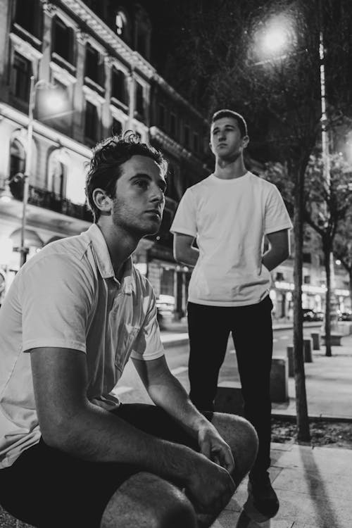 Two men sitting on the street in black and white