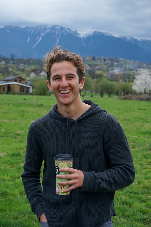 A smiling young man holding a coffee cup in front of a mountain