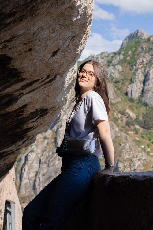 A woman in jeans and glasses is standing on a rock