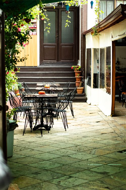 Free Cozy outdoor cafe setting with elegant metal chairs and potted plants, perfect for a relaxing urban escape. Stock Photo
