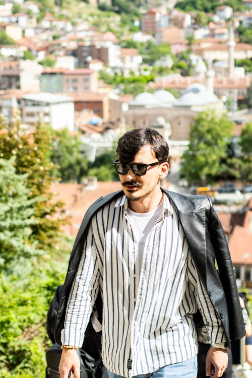 A man in a striped shirt and sunglasses walking down a street