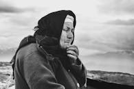 这是一幅黑白肖像，画面中一位老年妇女站在山脉背景前