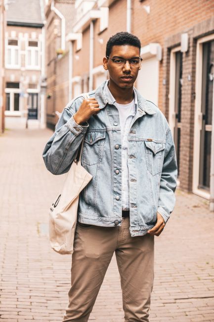 Stylish young man posing in urban setting with a denim jacket and casual outfit.