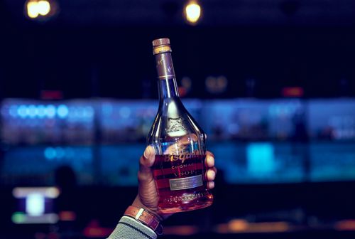Free A close-up of a hand holding a cognac bottle against a vibrant bar backdrop. Stock Photo
