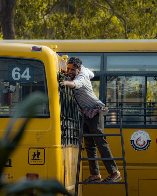 Free A worker on a ladder performing maintenance on a yellow school bus during the day. Stock Photo