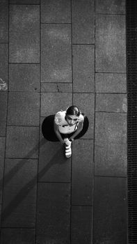 Black and white portrait of a woman sitting on pavement from an aerial view.
