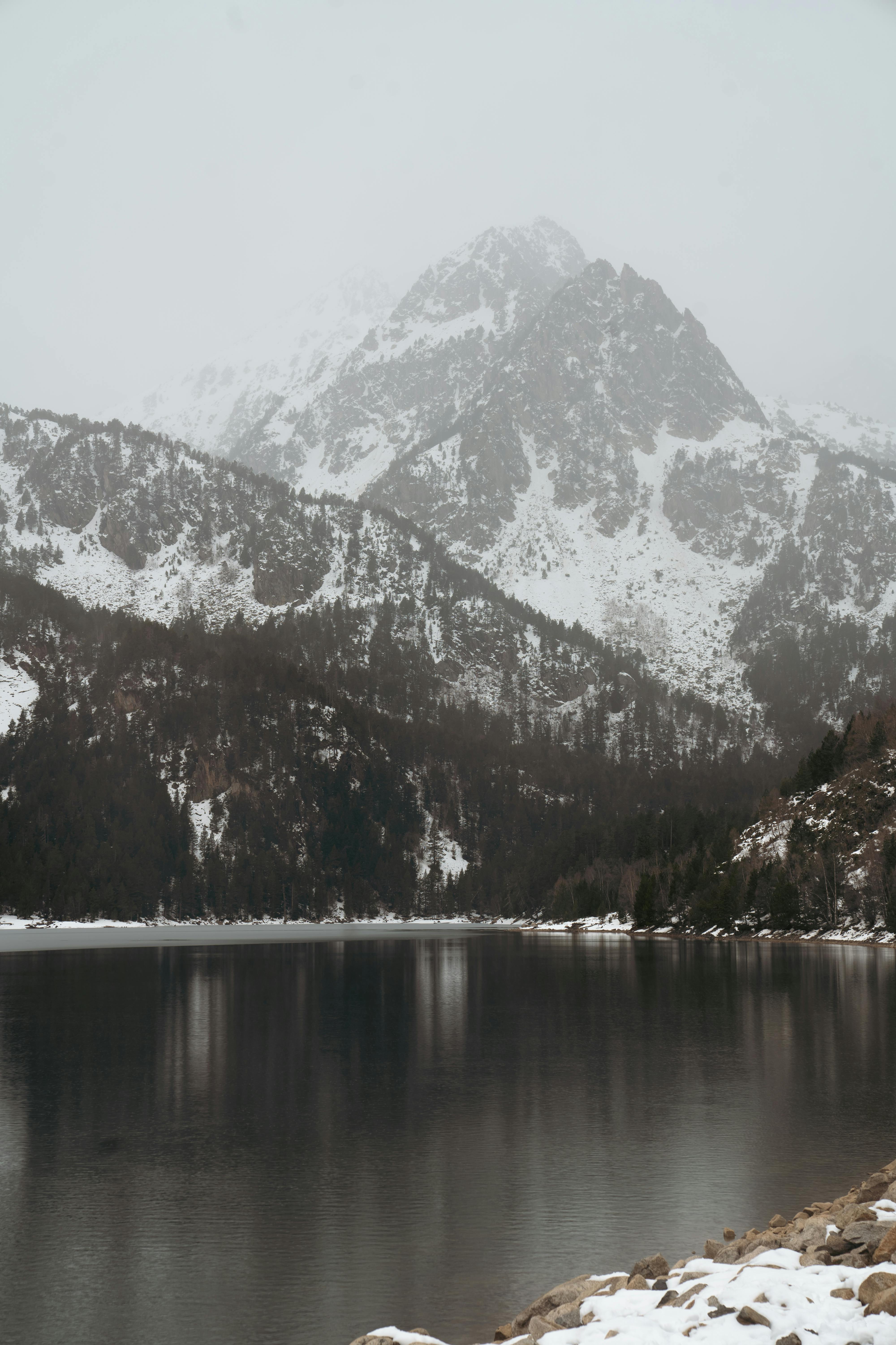 A stunning snowy mountain landscape with a tranquil lake and misty atmosphere.