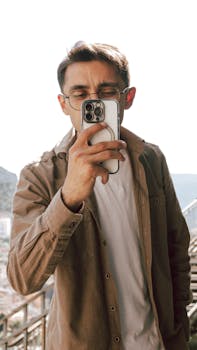Young man taking a selfie with a smartphone outdoors in Amasya, Türkiye, wearing eyeglasses.
