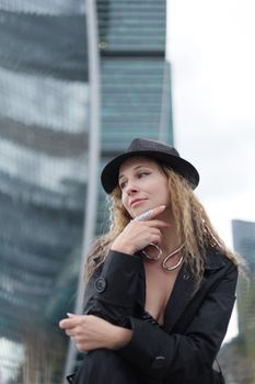 Chic woman in a black outfit and hat posing confidently against a modern skyscraper backdrop.