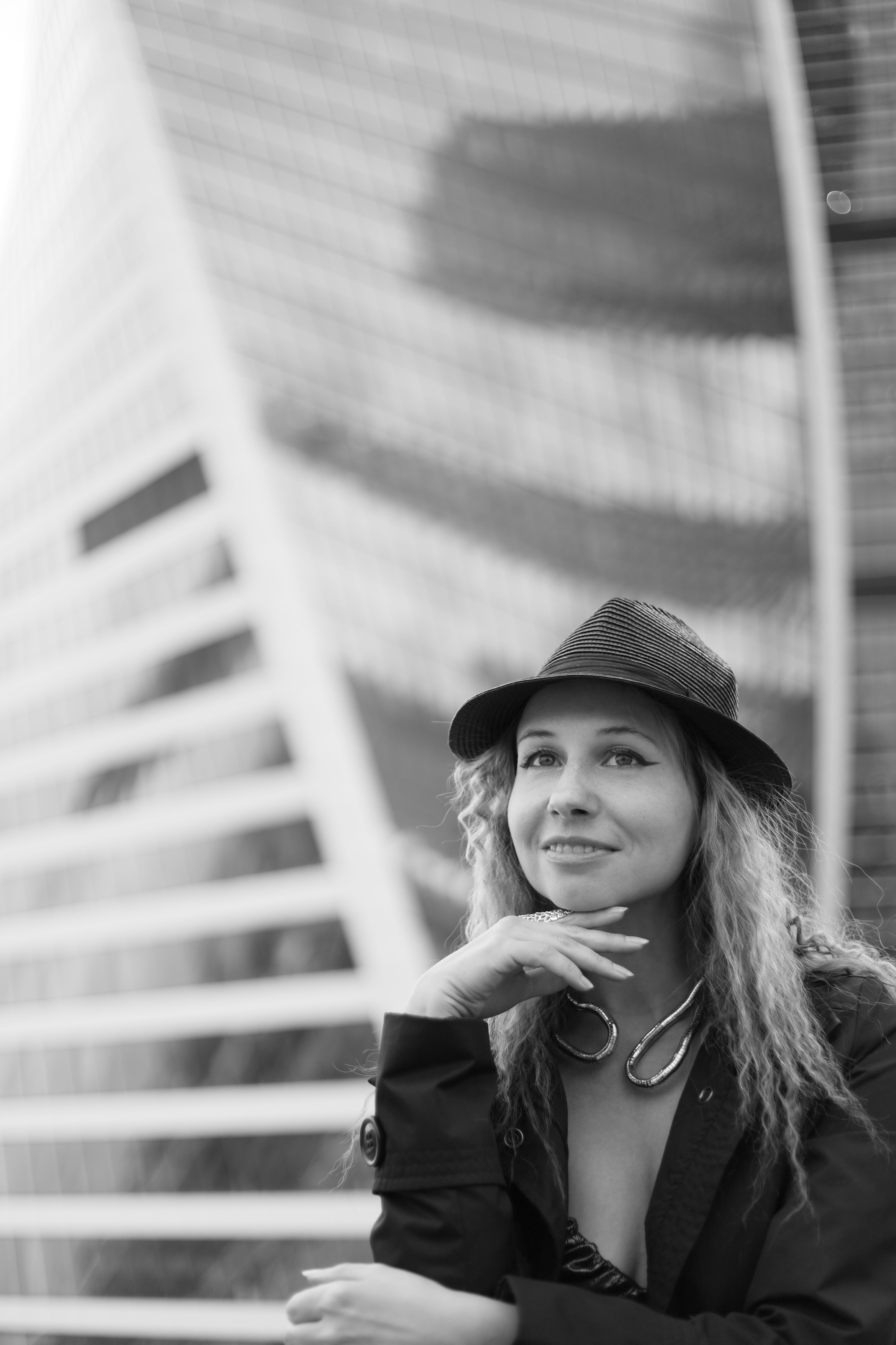 Elegant black and white portrait of a woman in a hat, posing in an urban environment.