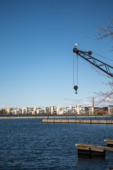 Urban waterfront scene in Lahti, Finland, showcasing a crane and buildings across the water.