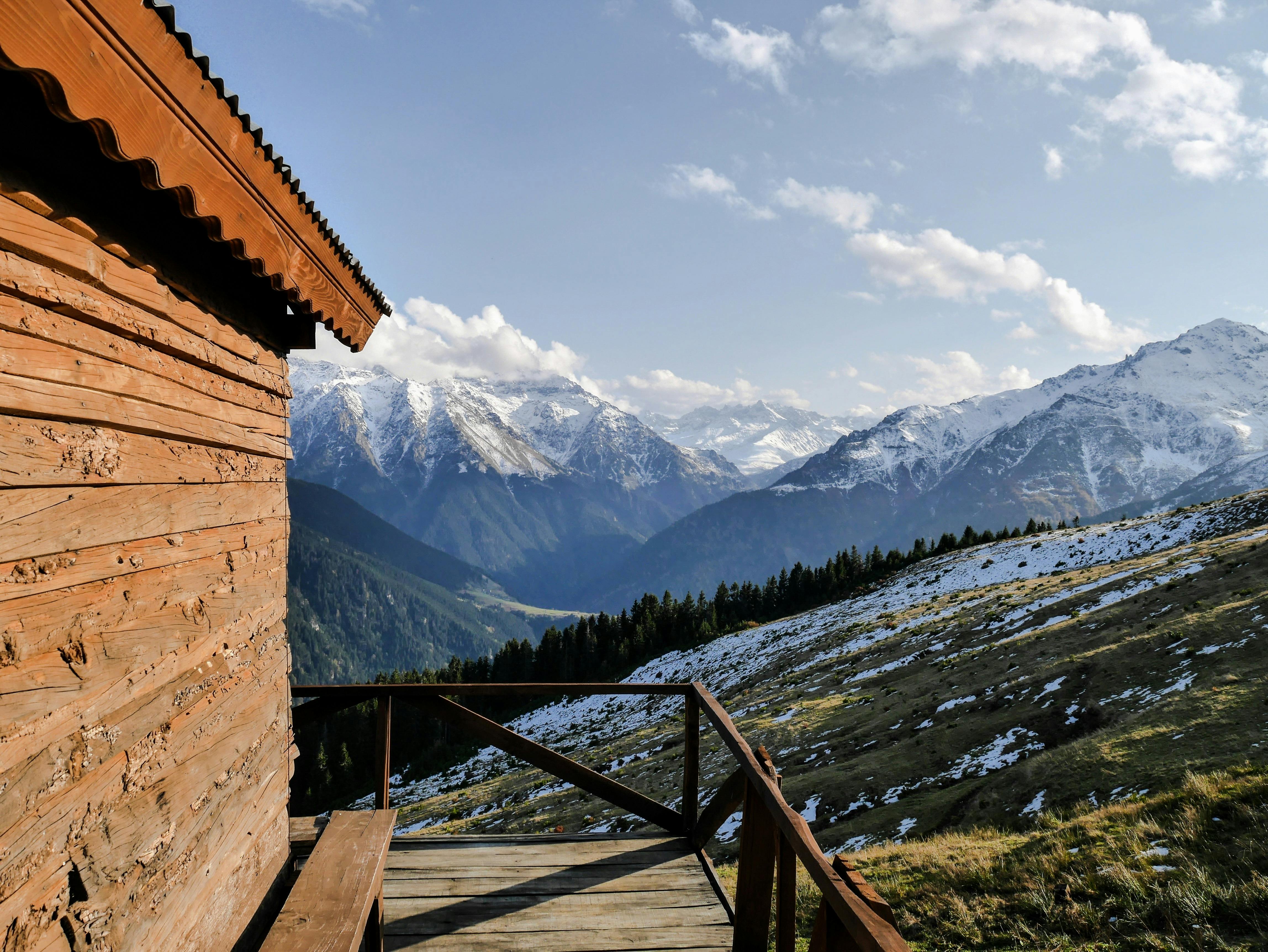 Serene mountain view from a wooden cabin's porch with snow-dusted peaks and clear sky.