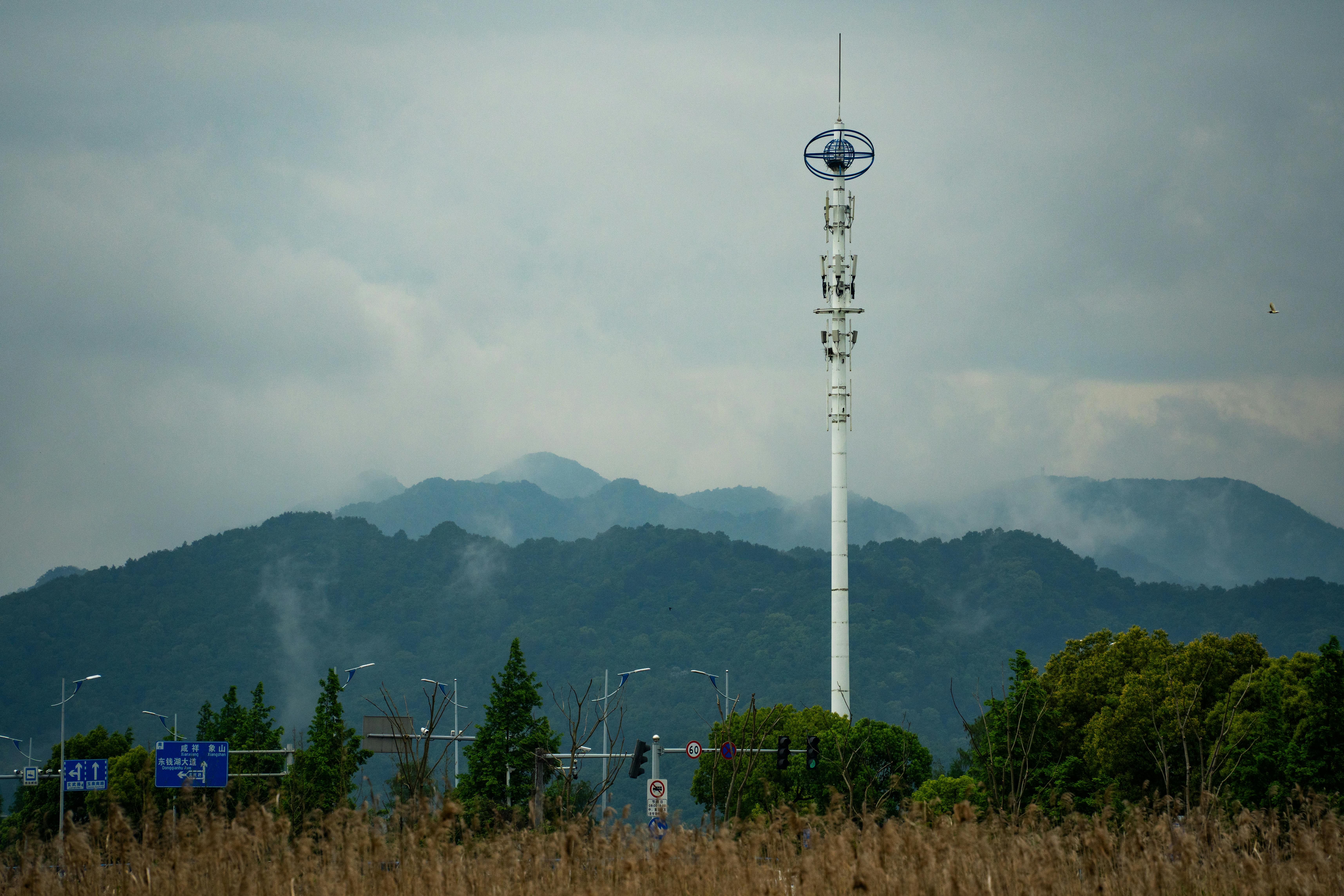 Telecommunications tower with cloudy sky and mountain range in the background.