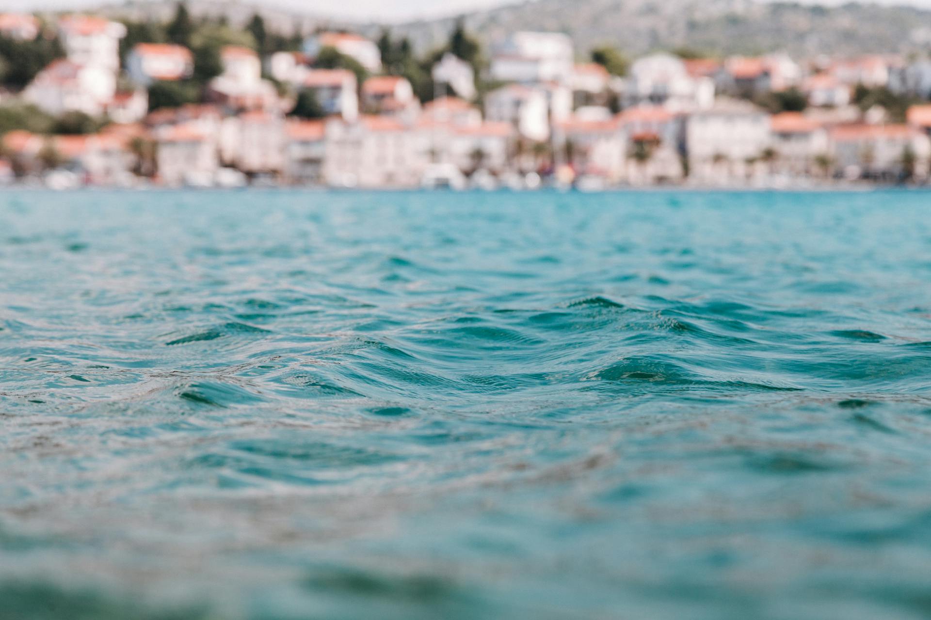 Tranquil ocean ripples with a blurred coastal town in the background, showcasing serene marine beauty.
