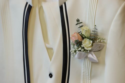 Free Detailed close-up of an elegant white suit adorned with a floral boutonniere, ideal for wedding photography. Stock Photo