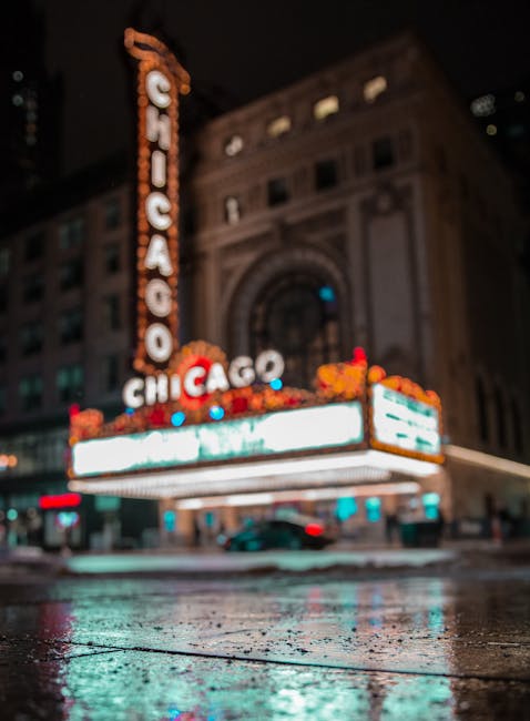 Iconic Chicago Theater illuminated with neon lights reflecting on wet pavement at night.