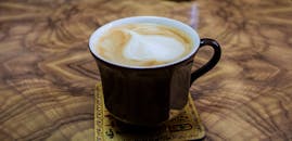 深色马克杯里装着一杯奶油卡布奇诺，配着拿铁艺术品，放在质朴的木桌上