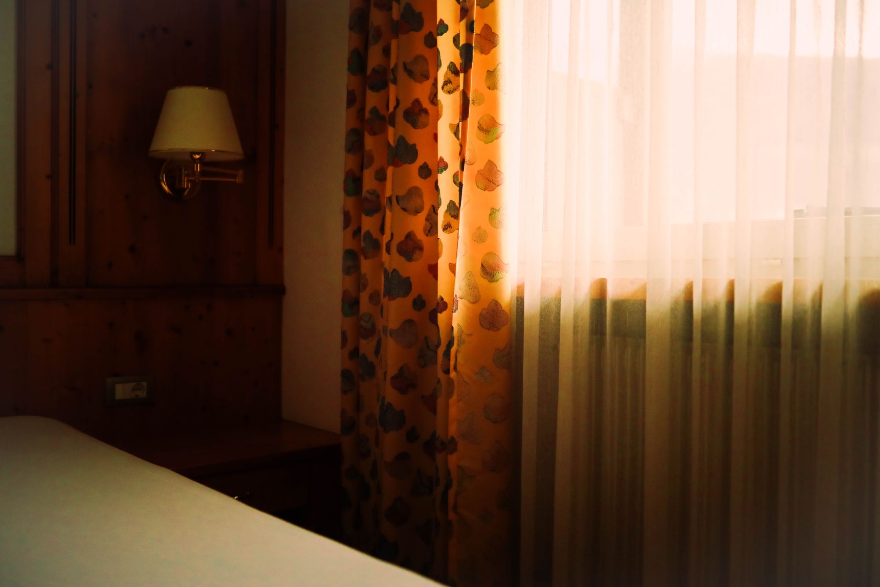 Bedroom filled with strong directional sunlight across pale walls, bedding and a timber floor