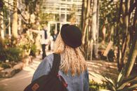 秋天，一位背着背包、戴着帽子的女士走过阳光明媚的花园