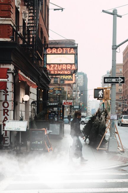 A man crosses a foggy street in New York City, surrounded by urban architecture and signs.