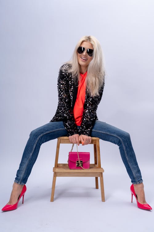 A blonde woman sitting on a chair with pink shoes and a bag