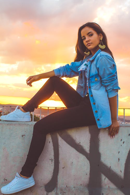 Photo of Posing Woman Sitting on Stone Railing During Golden Hour