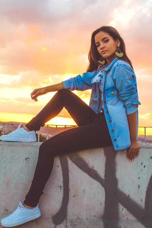 Photo of Posing Woman Sitting on Stone Railing During Golden Hour