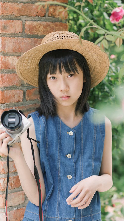 A girl in a hat and denim dress holding a camera