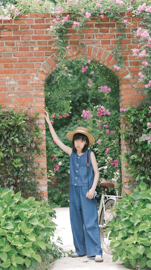 A girl in overalls standing in front of a brick wall