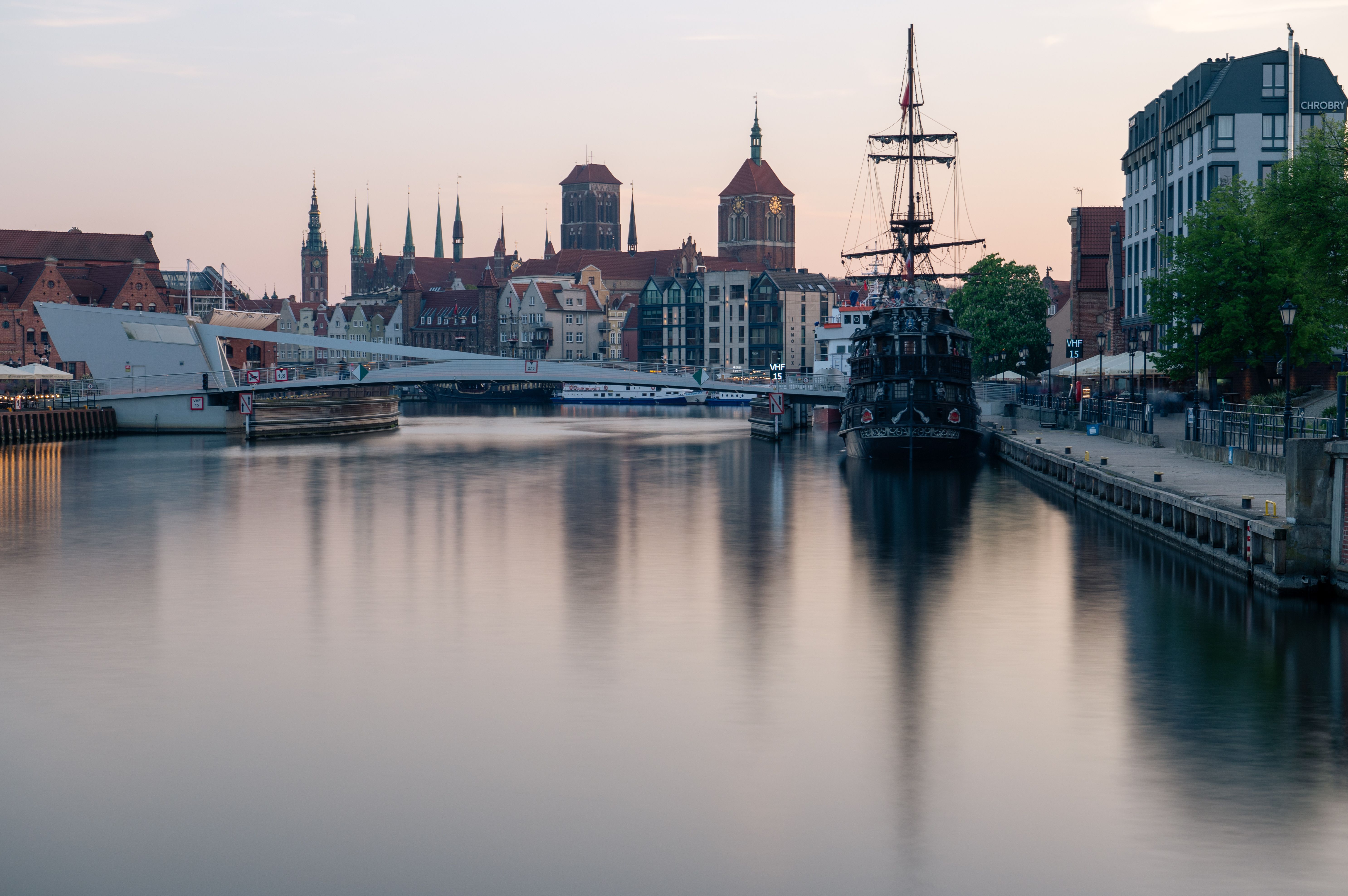 Captivating view of Gdańsk's historic skyline with a classic ship and bridge under a serene sunset.