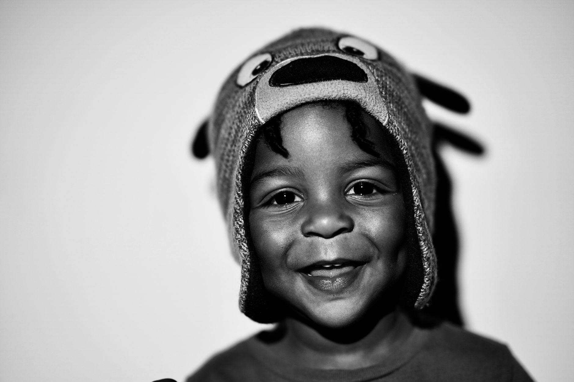 A black and white photo capturing the joy of a child wearing a playful animal hat with a delightful smile.