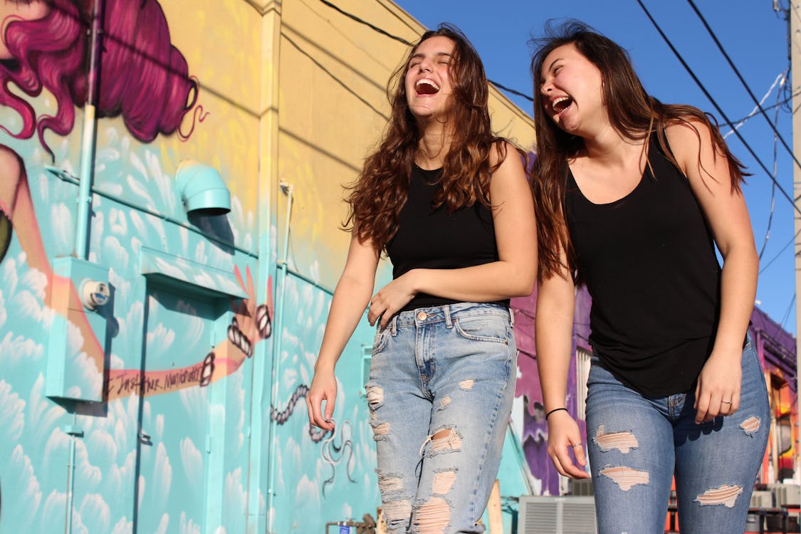 Foto Dua Wanita Tertawa Berjalan Melewati Dinding Grafiti