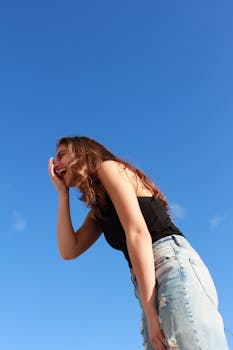 一位年轻女子身着休闲装，在户外对着鲜艳的蓝天欢笑，散发着幸福的光芒