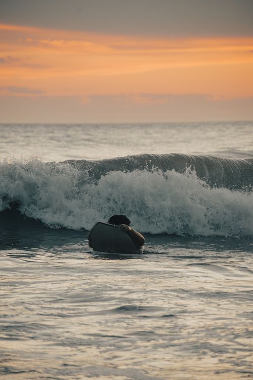 Free A surfer wrestling with powerful waves during a stunning sunset at sea. Stock Photo