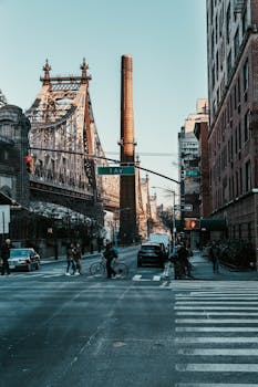 People and vehicles at a bustling New York City intersection near the iconic Queensboro Bridge.