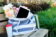 公园长凳上，一个装有平板电脑的条纹手提袋旁摆放着鲜花，构成了理想的现代户外场景